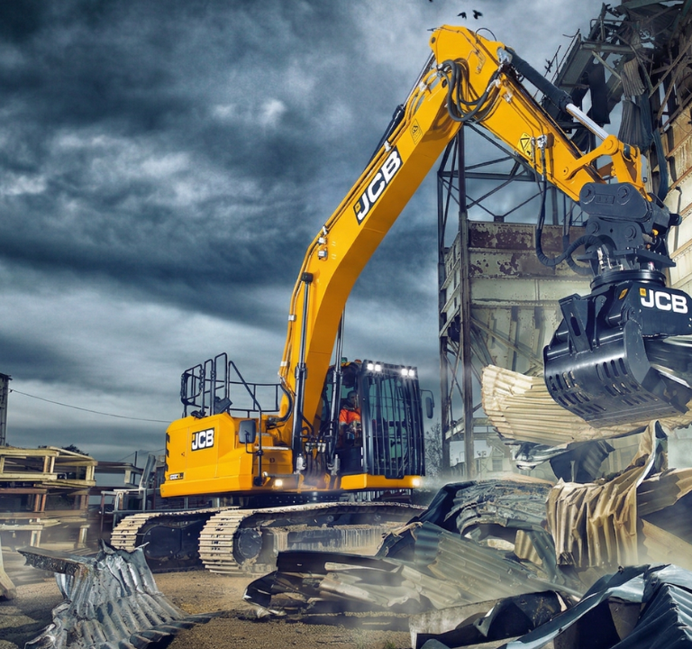 JCB-merkkinen kaivinkone, joka on varustettu purkukouralla, on juuri nostamassa tai repimässä irti suurta kasaa aaltopeltiä ja muuta rakennusjätettä.